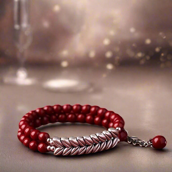 Red beaded bracelet with a silver braided section on a white background