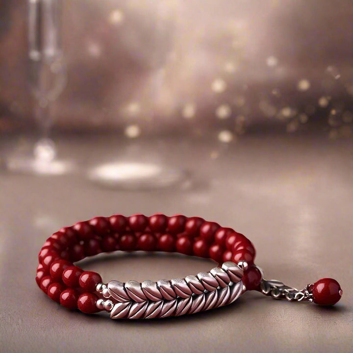 Red beaded bracelet with a silver braided section on a white background