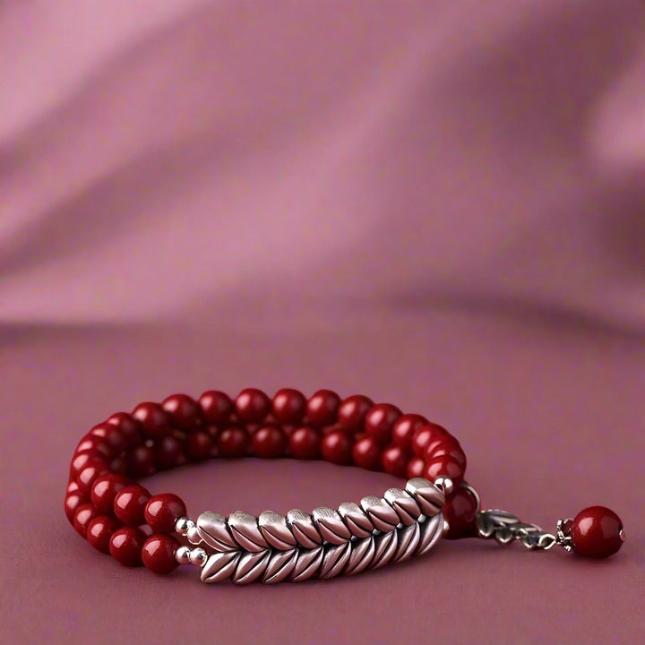 Red beaded bracelet with silver braided design on a red background, featuring the brand 'Anshun Sui'.
