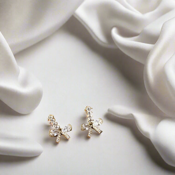 Bow-shaped earrings on a wooden surface with a piece of paper in the background